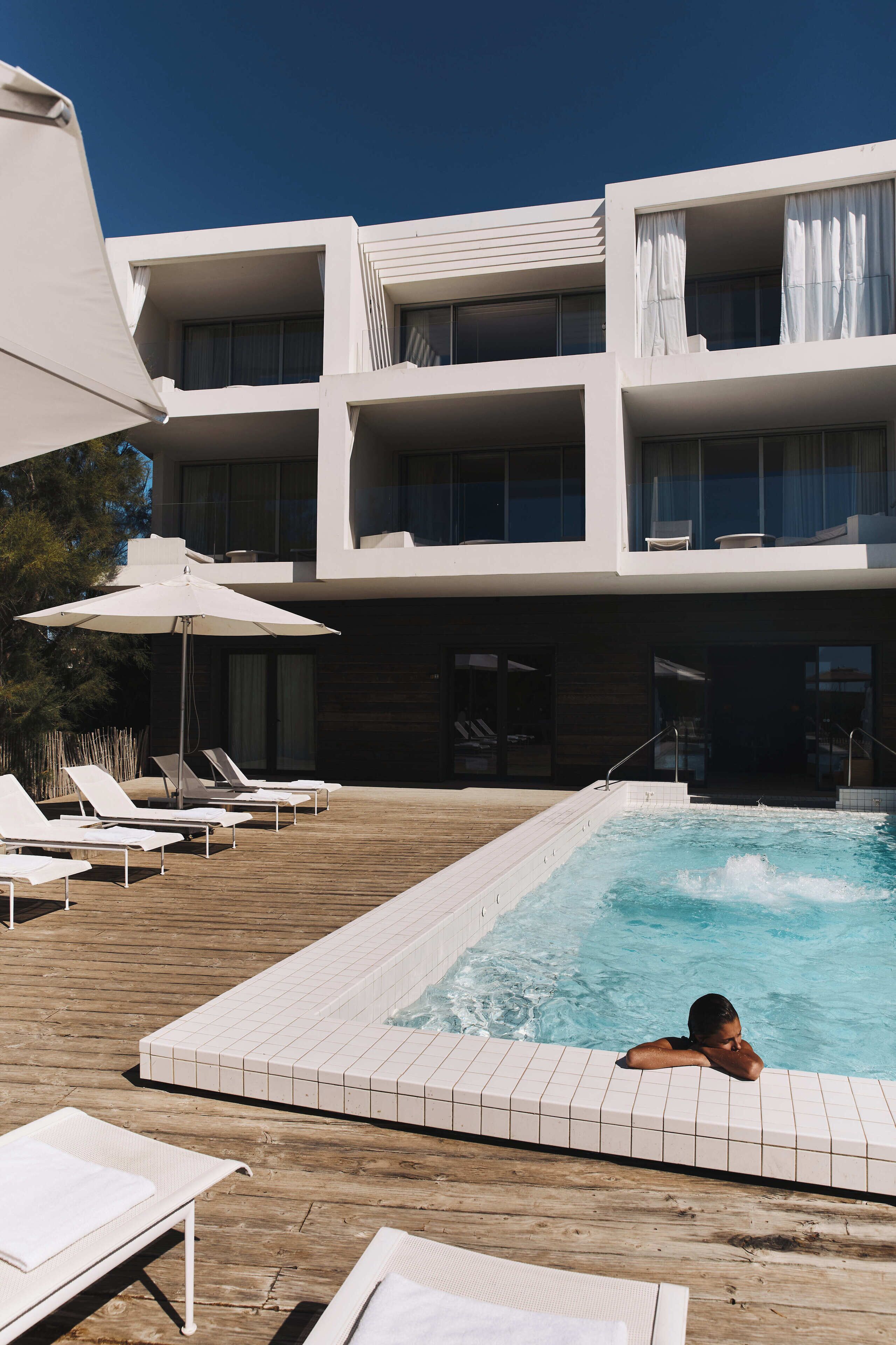 Un hotel modern amb piscina al terrat, gandules i un cel blau clar.