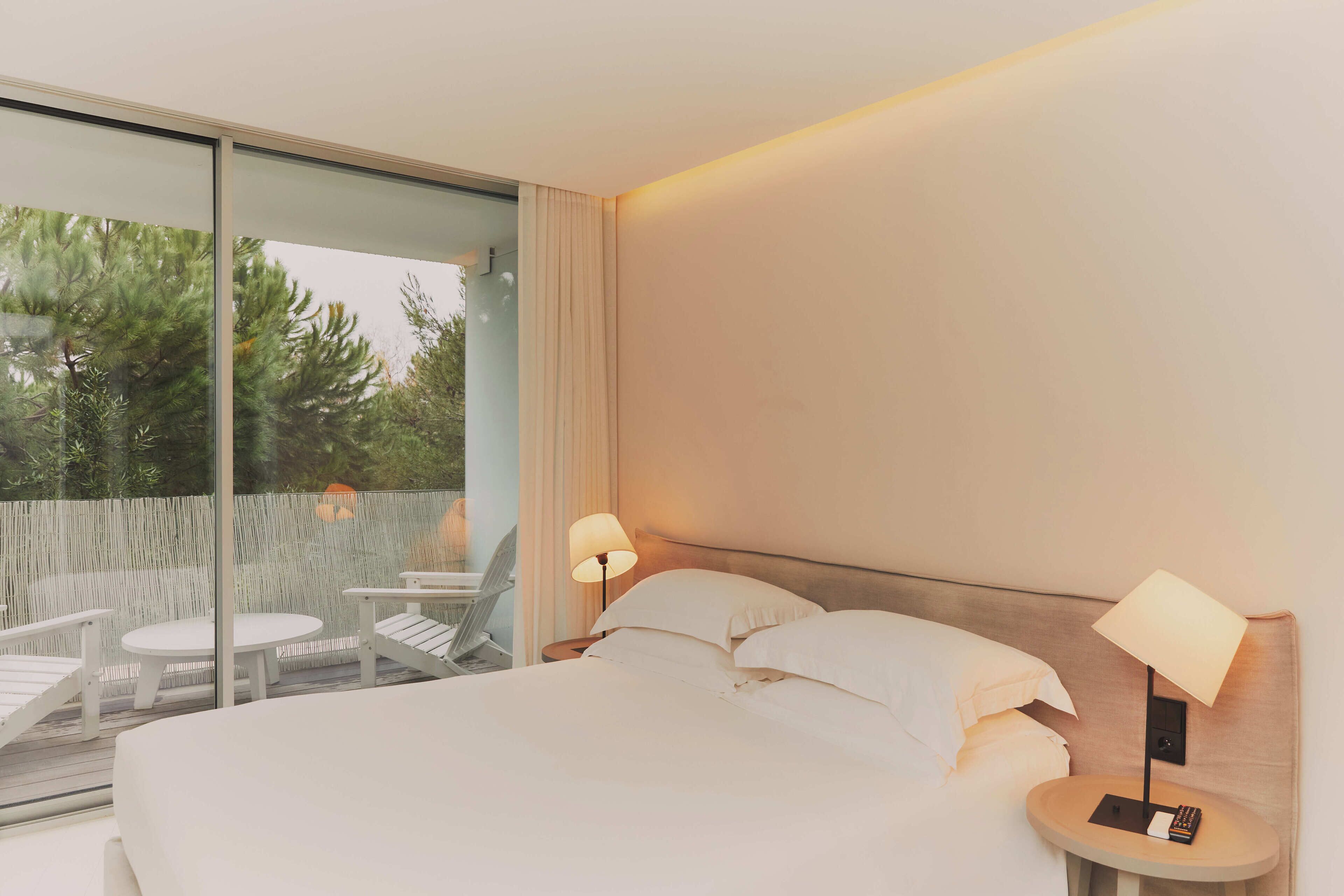 A hotel room with a large bed, two bedside tables with lamps, a small round table, and a chair.
