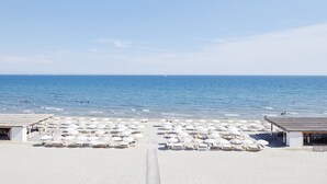 A beach with rows of white sunbeds and umbrellas, a clear sky, and the ocean in the background. - Hôtel Plage Palace & Spa (Palavas-les-Flots)