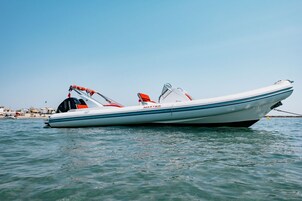 A small, white motorboat with a red and black canopy, floating on calm water.