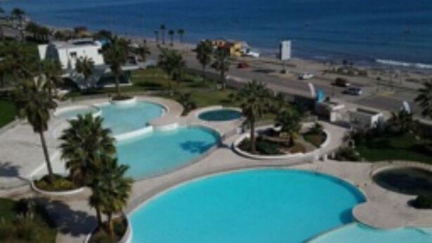A resort with multiple swimming pools surrounded by palm trees and a view of the ocean.