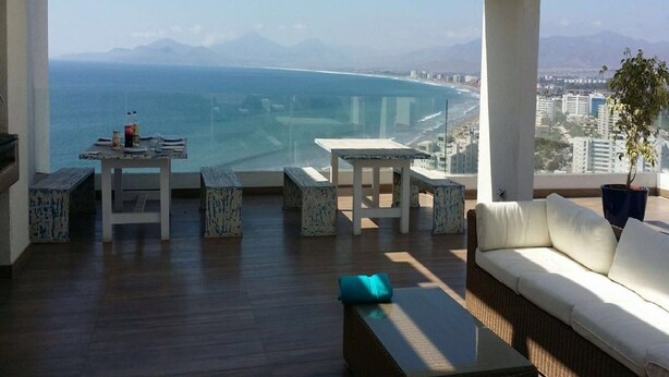 Ruim balkon met uitzicht op zee en bergen, voorzien van een bank, tafels en stoelen.
