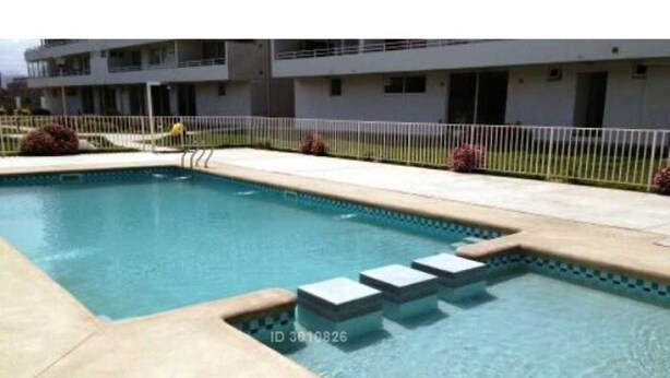 A swimming pool with steps leading into it, surrounded by a fence and a building in the background. - Departamento Los Lucumos de La Serena (La Serena)