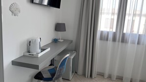 Une chambre d’hôtel moderne équipée d’un téléviseur à écran plat, d’un bureau avec une lampe, d’une chaise et d’une fenêtre avec des rideaux légers.