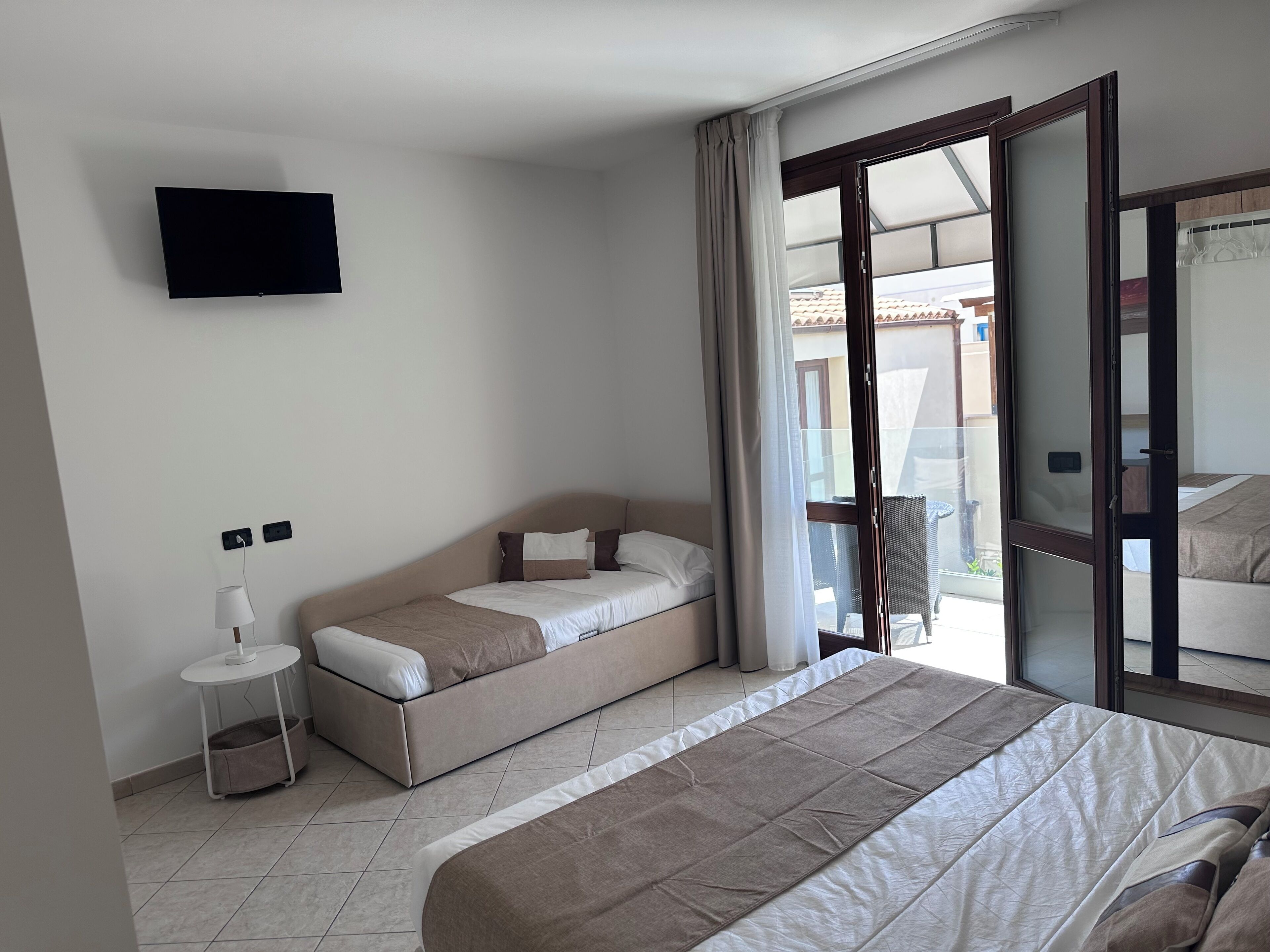 Un dormitorio con cama, sofá cama, televisor montado en la pared y ventana con cortinas.