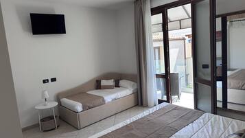 Un dormitorio con cama, sofá cama, televisor montado en la pared y ventana con cortinas.
