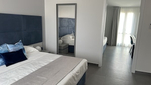 Une chambre d’hôtel moderne avec un grand lit, une table de chevet, un miroir et une vue sur l’espace repas.