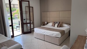 Une chambre d’hôtel dotée d’un grand lit, d’un bureau, d’une chaise, d’une table de chevet et d’une porte-fenêtre coulissante donnant sur un espace extérieur.