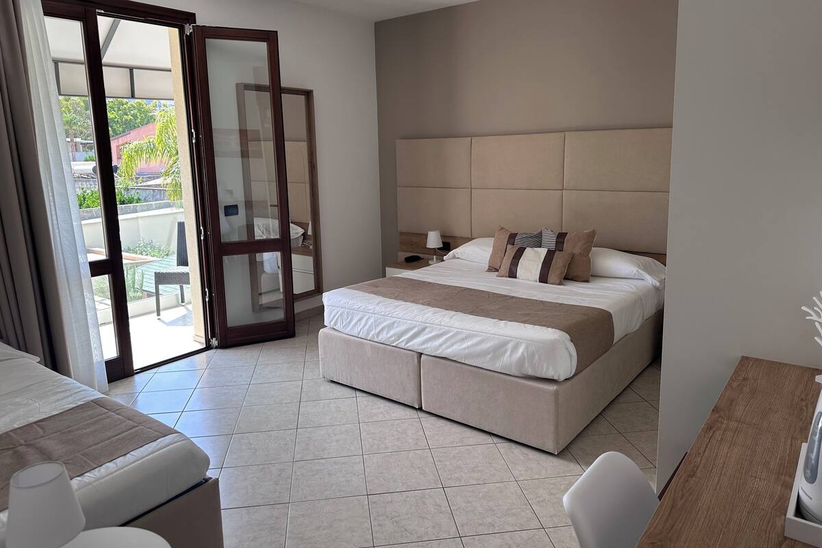 Une chambre d’hôtel dotée d’un grand lit, d’un bureau, d’une chaise, d’une table de chevet et d’une porte-fenêtre coulissante donnant sur un espace extérieur.