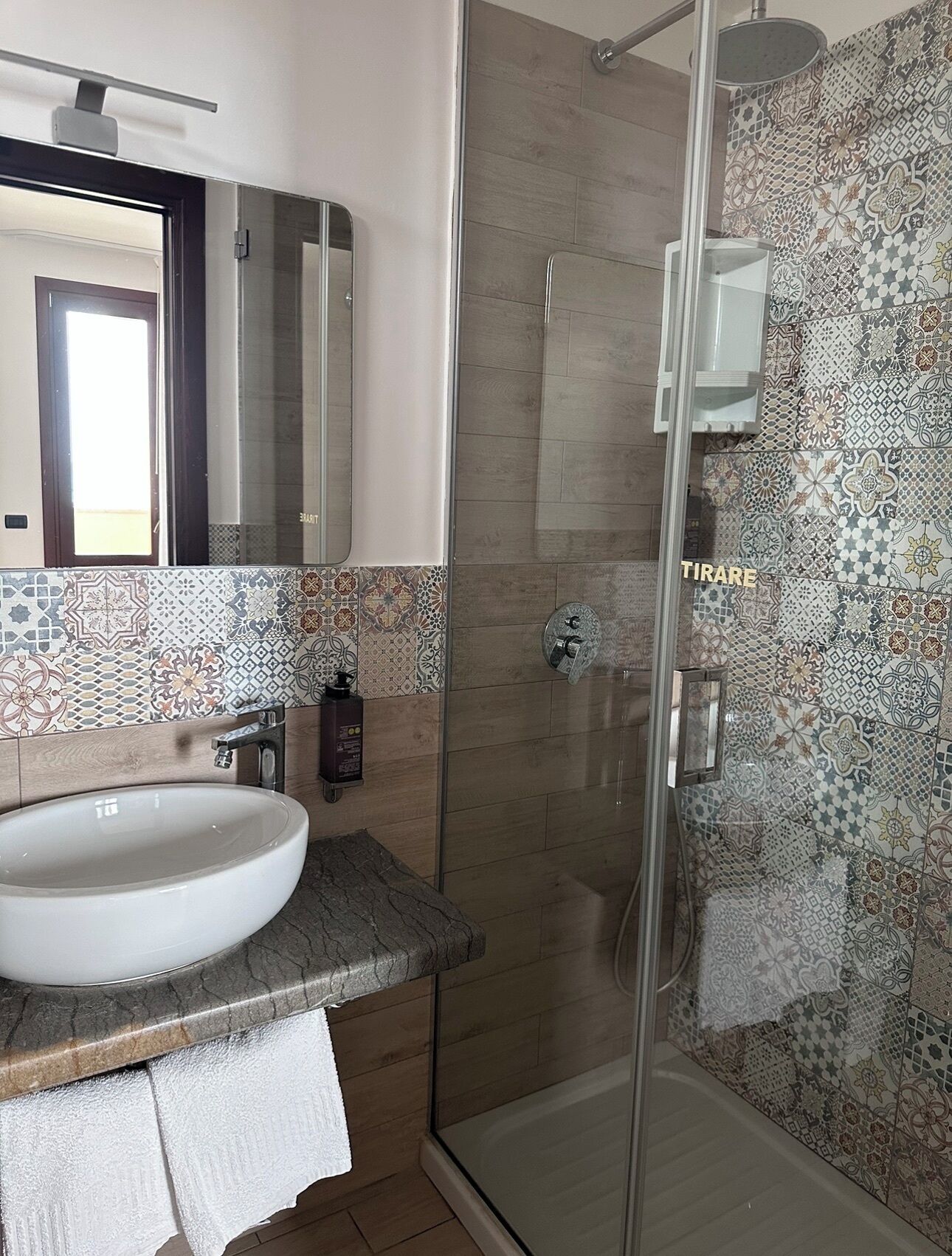 Un bagno con doccia vetrata, lavandino bianco e schienale piastrellato.