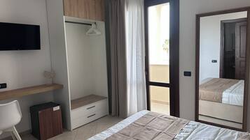 Una habitación de hotel con cama, escritorio, armario, televisor y balcón.