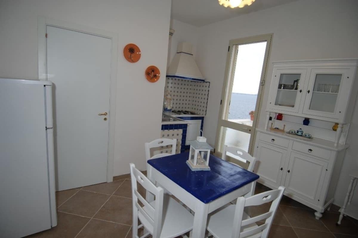 Una cocina con armarios blancos, una mesa azul y vistas al mar a través de una ventana.