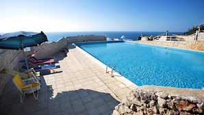 A swimming pool with lounge chairs and umbrellas, a stone wall, and a view of the sea. - Dada, Pool Residence (Gagliano del Capo)