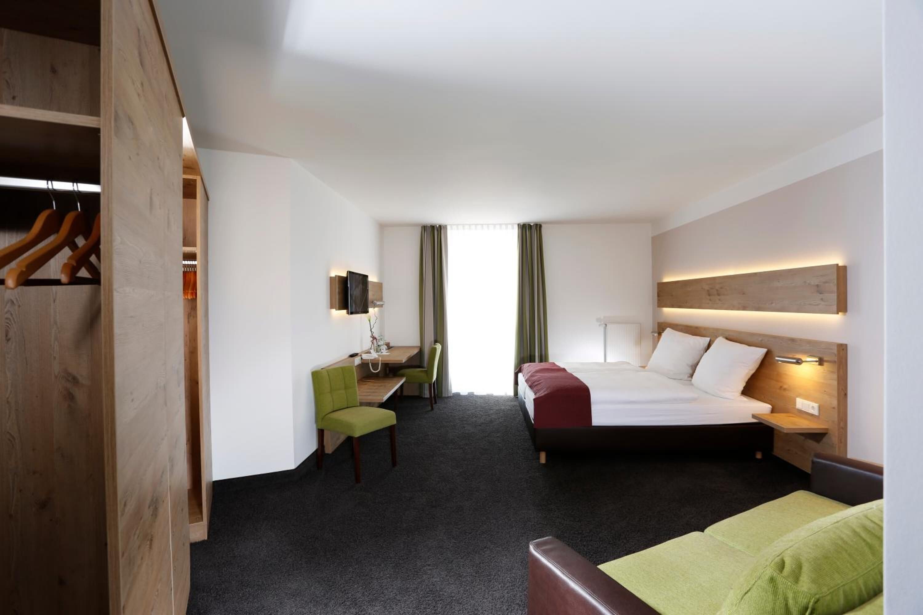 A hotel room with a bed, desk, chair, and wardrobe.