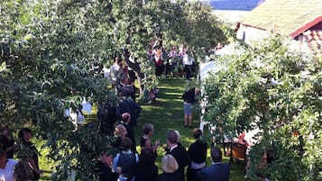 A group of people gathered outdoors, possibly at a social event, with trees and a building in the background.