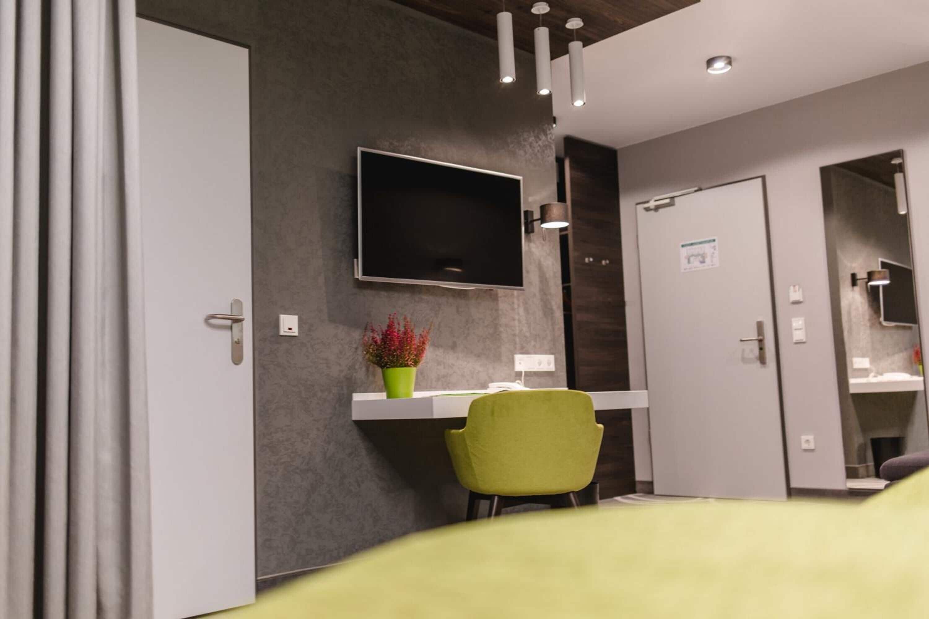 Ein modernes Hotelzimmer mit einem an der Wand befestigten Flachbildfernseher, einem Schreibtisch mit Stuhl und einer Tür zu einem Badezimmer.