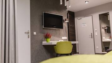 Una habitació d'hotel moderna amb televisió de pantalla plana penjada a la paret, una taula amb cadira, i una porta que dóna a un bany.