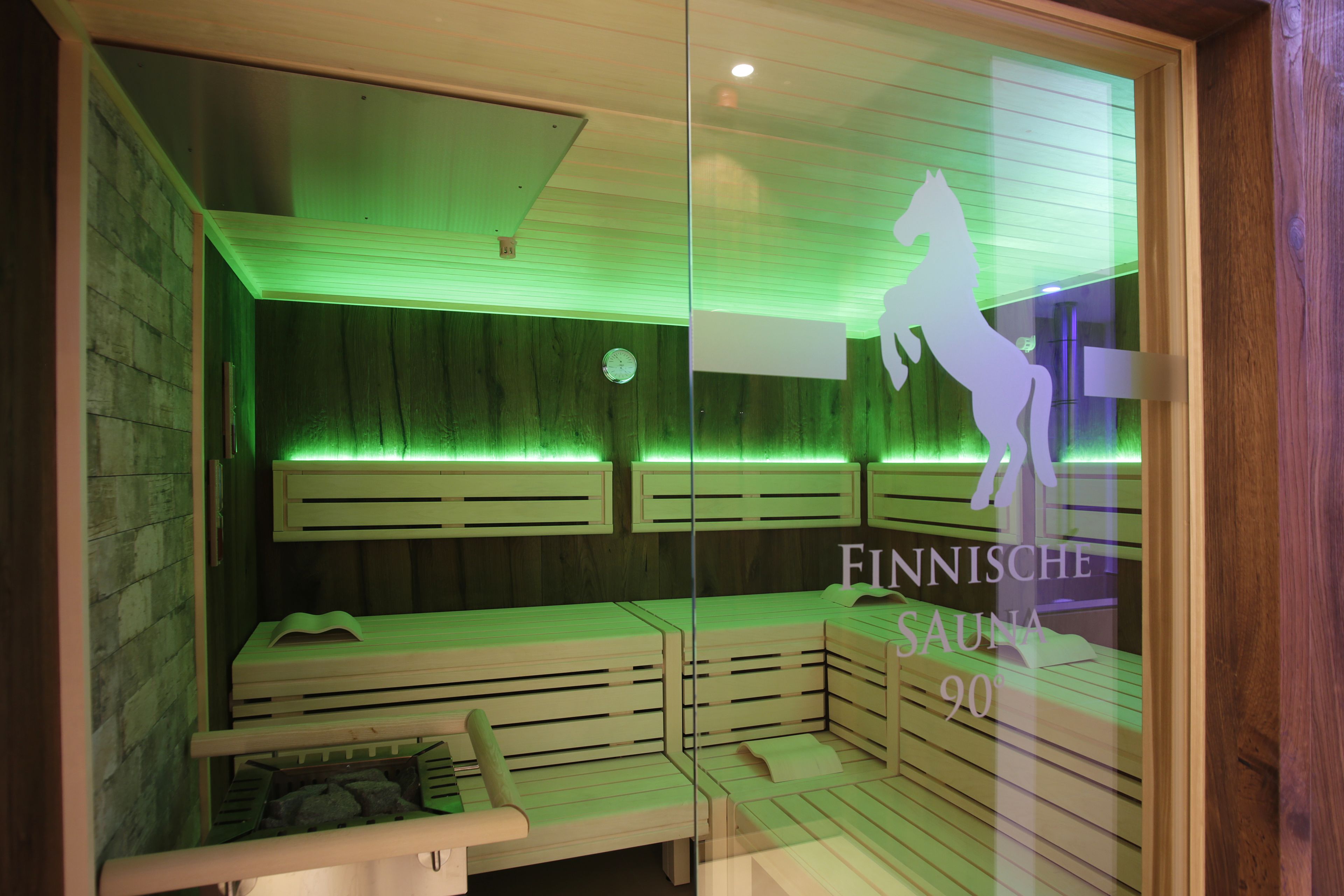 A sauna room with wooden benches and a glass wall displaying a horse silhouette.