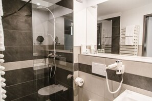 A modern bathroom with a glass-enclosed shower, a toilet, and a sink with a hairdryer. - Hotel Restaurant Sachsenross (Norten-Hardenberg)