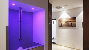 Een moderne badkamer met een verlichte douche in paarse tinten en een hal met een schilderij van een zonsondergang.