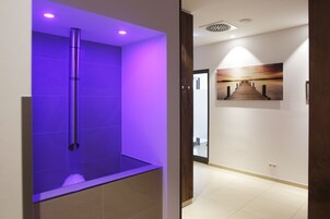 A modern bathroom with a purple-lit shower area and a hallway with a sunset painting.