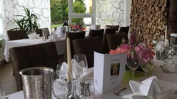 A dining table set with white tablecloths, silverware, and glassware, with a menu box and floral centerpiece.