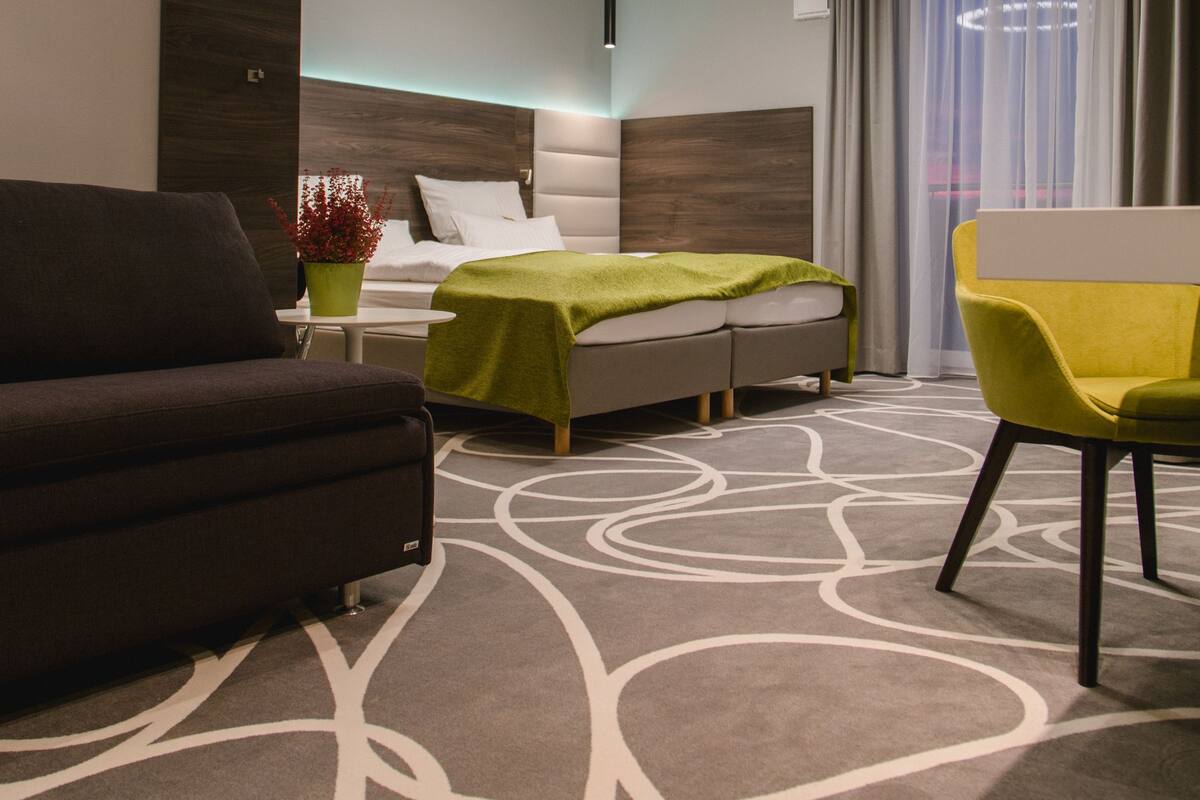 Een moderne hotelkamer met een bed, een bank, een stoel en een ronde plafondlamp.
