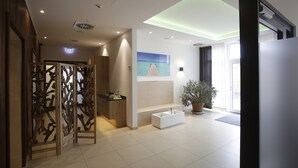 Een moderne hotellobby met een houten decoratief scherm, een wit receptiebalie, een groot raam met uitzicht en een potplant.