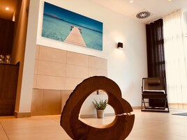 A modern lobby with a wooden sculpture, a painting of a pier, and a potted plant.