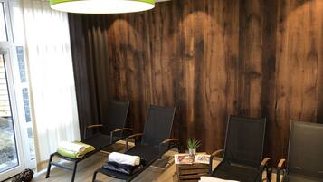 Ein Zimmer mit Holzpaneelen, schwarzen Lounge-Stühlen, einer grünen Lampe und einem Tisch mit Pflanze und Zeitschriften.