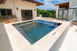 A rectangular swimming pool with a stone border, a wooden deck, and a covered patio area with outdoor furniture. - Grand Laguna Beach Properties by Calisto Stays (Sosúa)