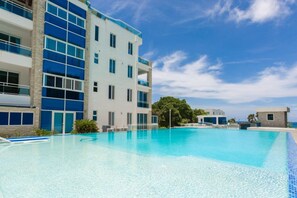 A modern hotel with a large swimming pool, multiple balconies, and a clear blue sky. - Grand Laguna Beach Properties by Calisto Stays (Sosúa)