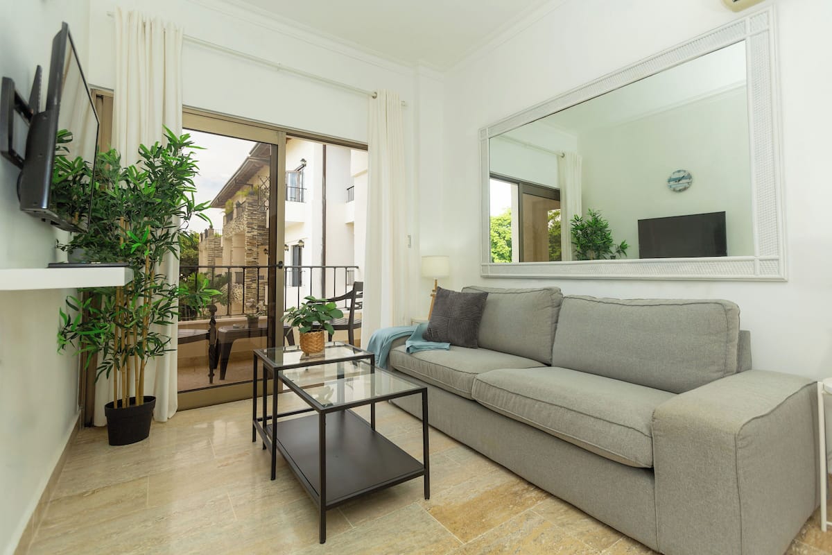Un salon avec un canapé, une table basse en verre, un téléviseur et des plantes en pot.