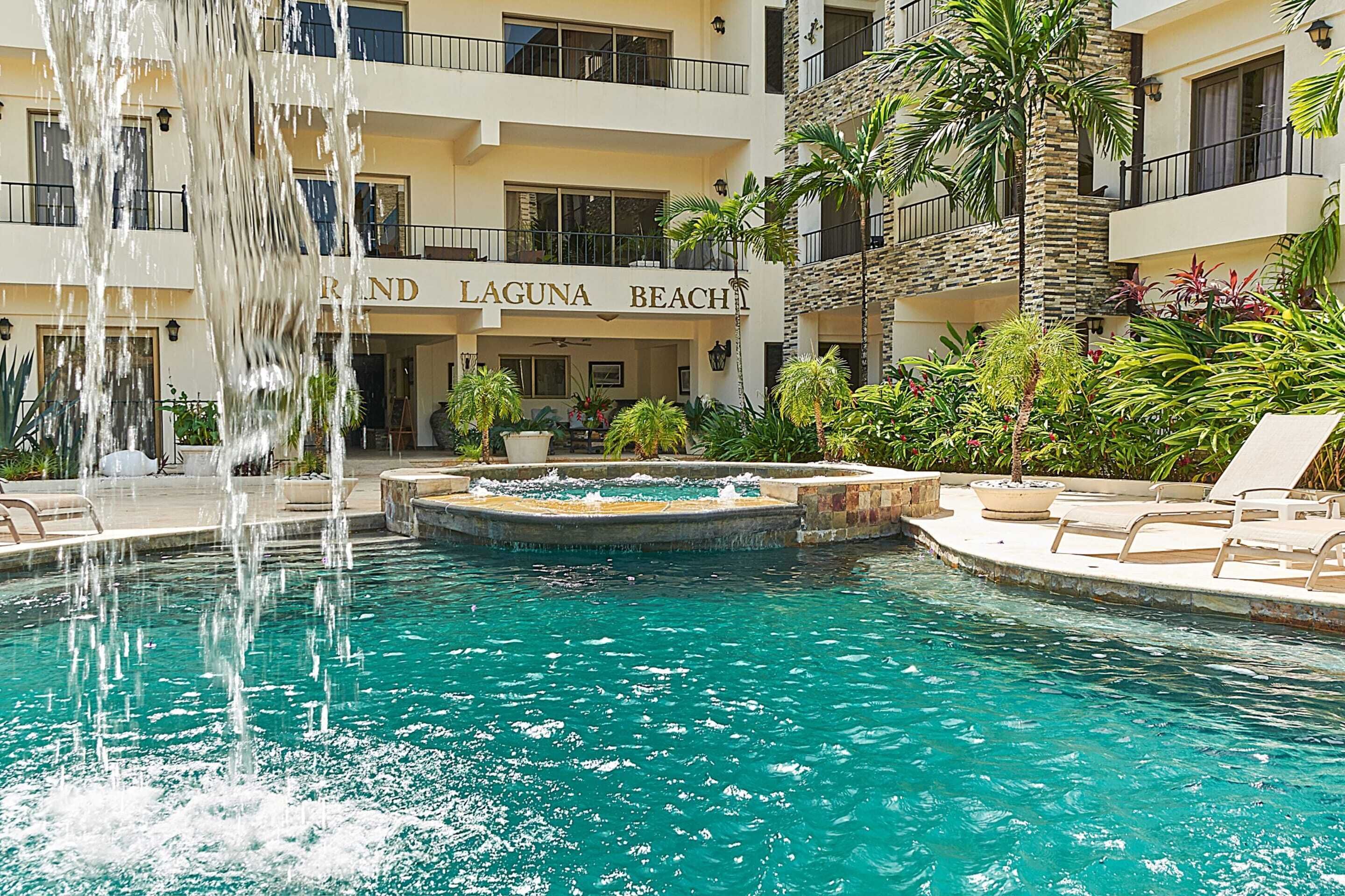 A hotel with a pool featuring a waterfall, surrounded by lush greenery and lounge chairs.