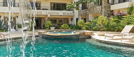 A hotel with a pool featuring a waterfall, surrounded by lush greenery and lounge chairs.