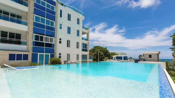 A modern hotel with a large swimming pool, multiple balconies, and a clear view of the ocean. - Grand Laguna Beach Properties by Calisto Stays (Sosúa)