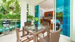 An outdoor dining area with wicker chairs and a glass table, a barbecue grill, and a view of the kitchen through a glass door. - Grand Laguna Beach Properties by Calisto Stays (Sosúa)