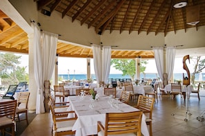 An outdoor dining area with wooden tables and chairs, white tablecloths, and a view of the sea. - Ocean Village 93 (Sosúa)
