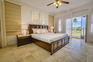 A bedroom with a large bed, two bedside tables, a ceiling fan, and a view of the outdoors. - Ocean Village 93 (Sosúa)