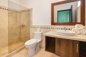 A modern bathroom with a glass-enclosed shower, a toilet, a sink with a mirror above, and neatly rolled towels.