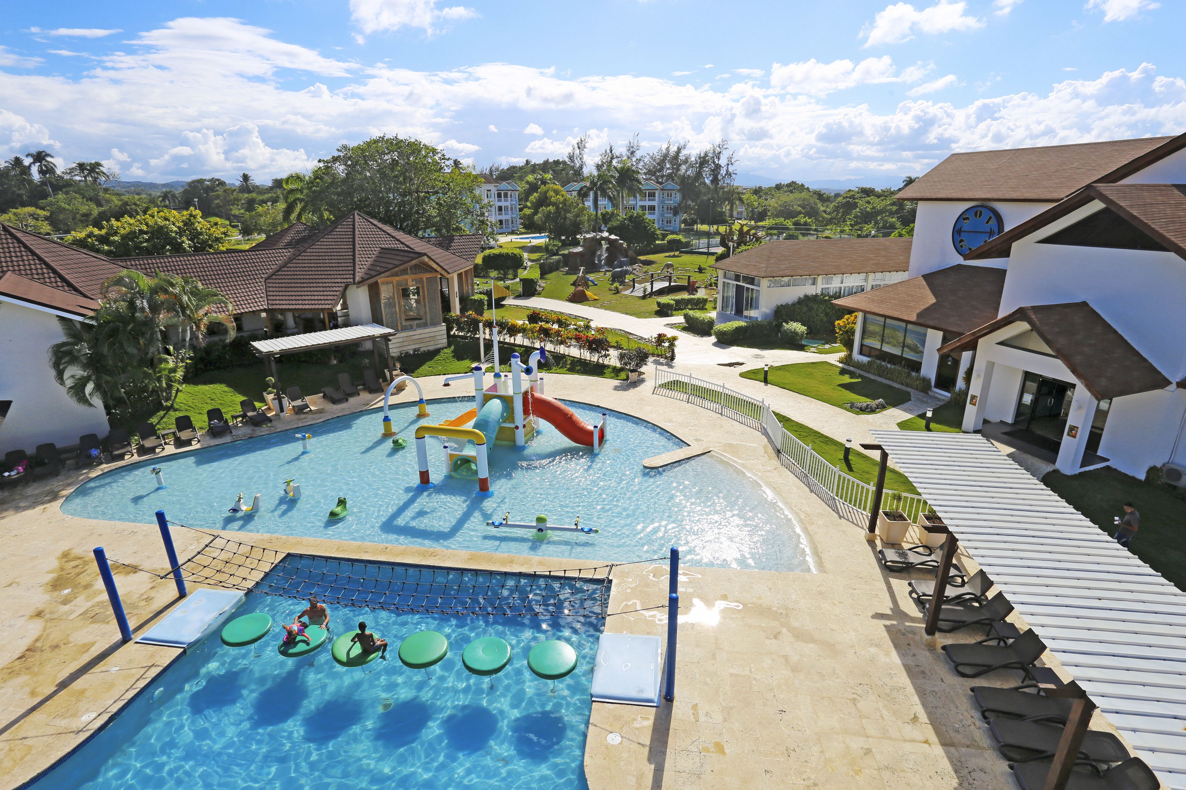 A swimming pool with a slide and play area, surrounded by houses and greenery.