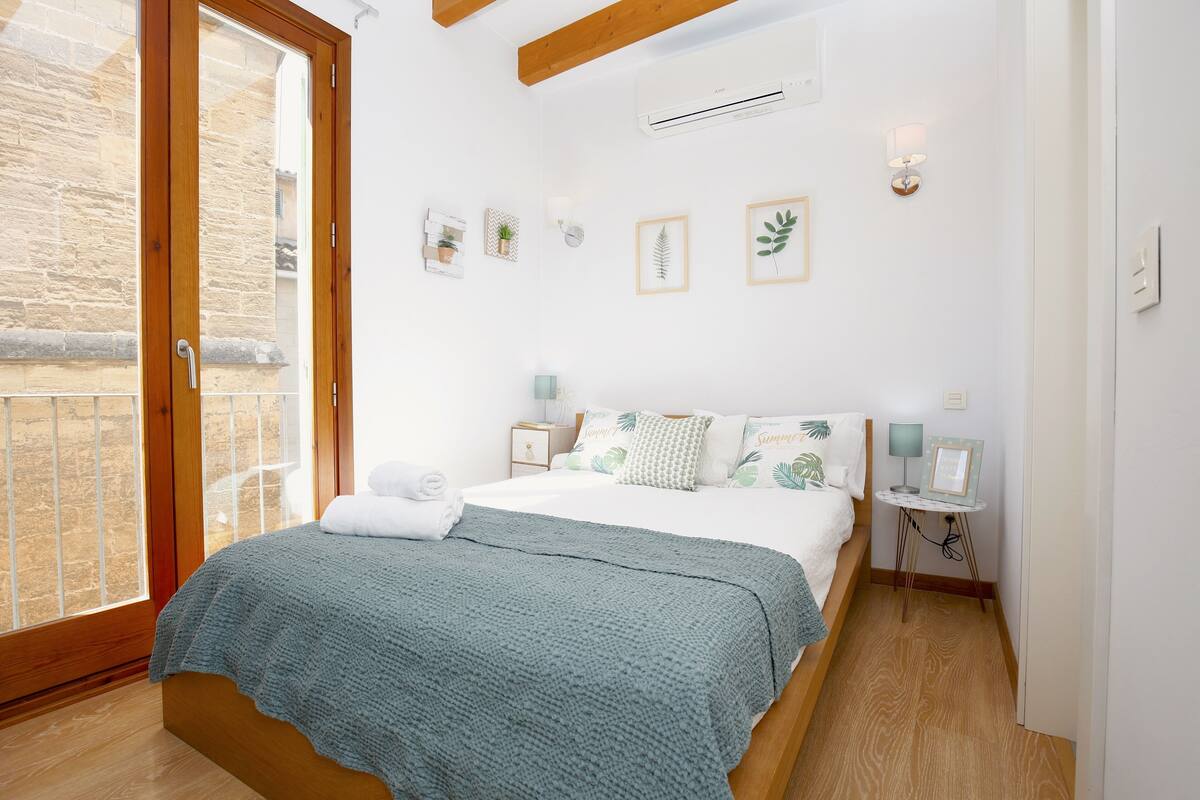 Ein Schlafzimmer mit einem Bett, Nachttischen, einem Fenster und einer Wand-Klimaanlage.