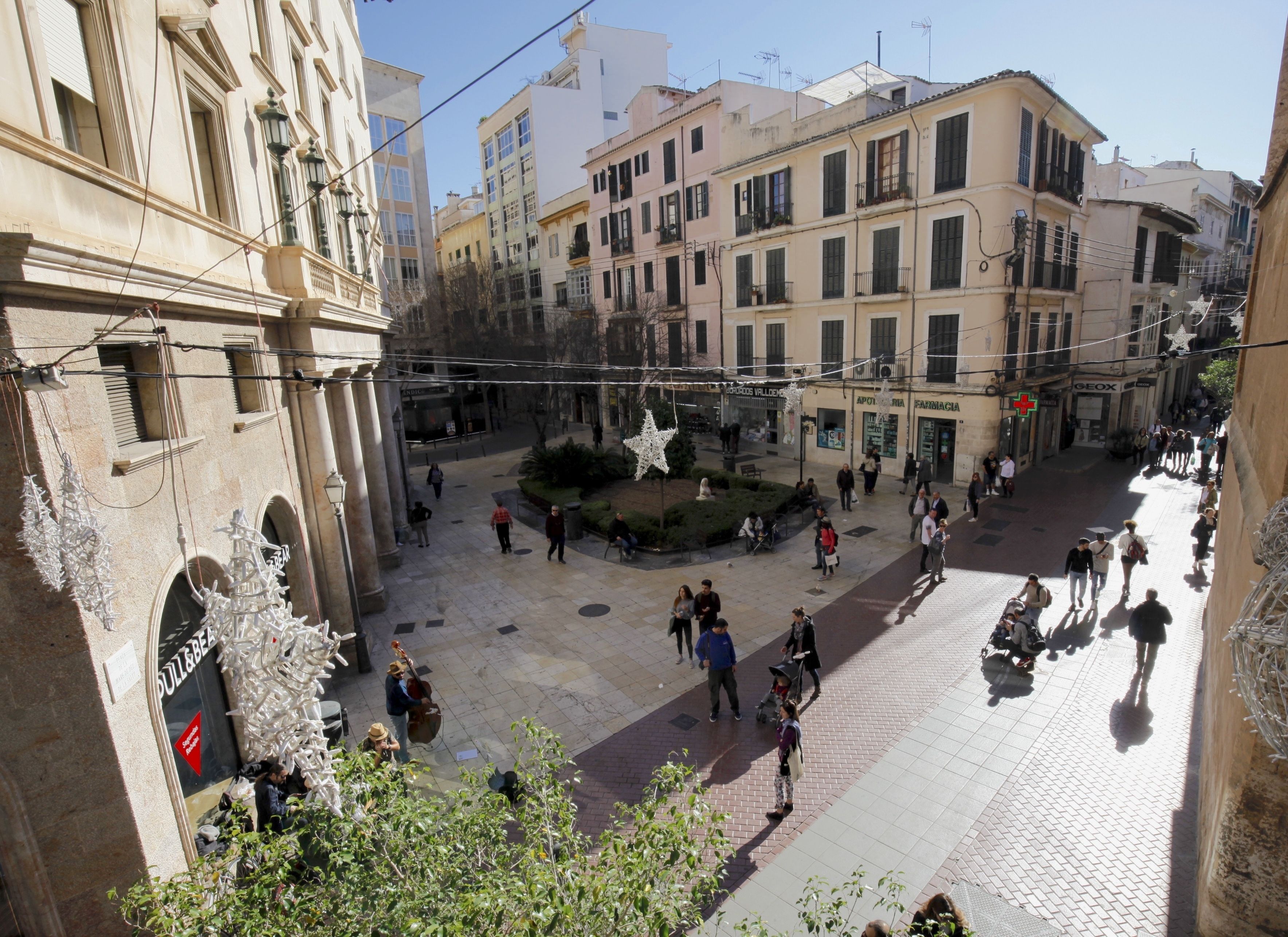 Una plaza pública con edificios históricos, una fuente y gente caminando.