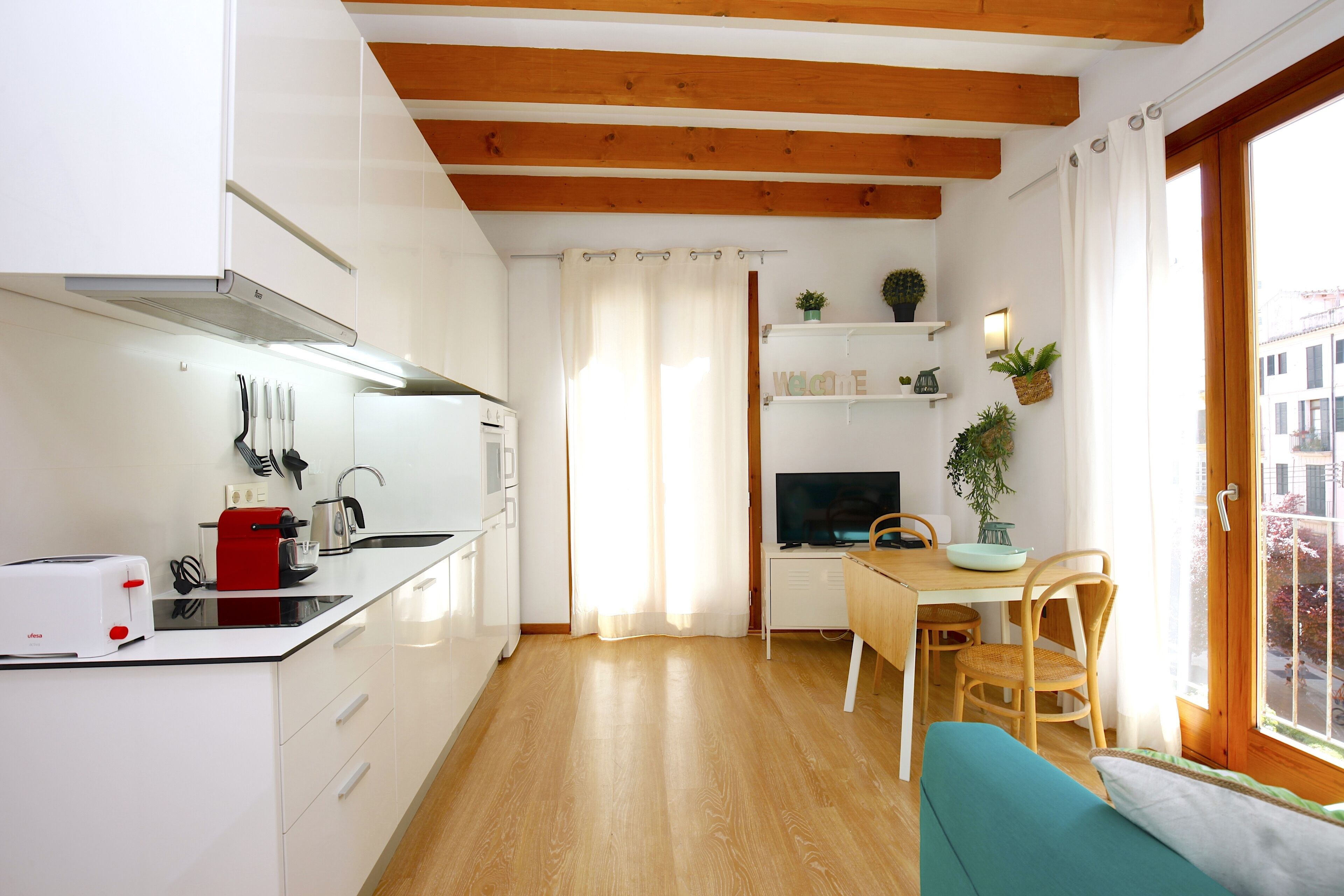 Een knus keukentje met witte kastjes, een houten plafond, een eethoek met een tafel en stoelen, en een raam met gordijnen.