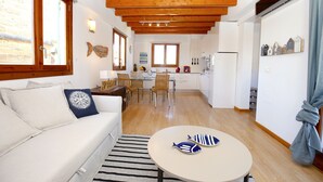 A modern kitchen with wooden beams, a dining area with a round table, and a living room with a sofa and striped rug. - Sant Miquel Homes - Turismo de Interior (Palma de Mallorca)