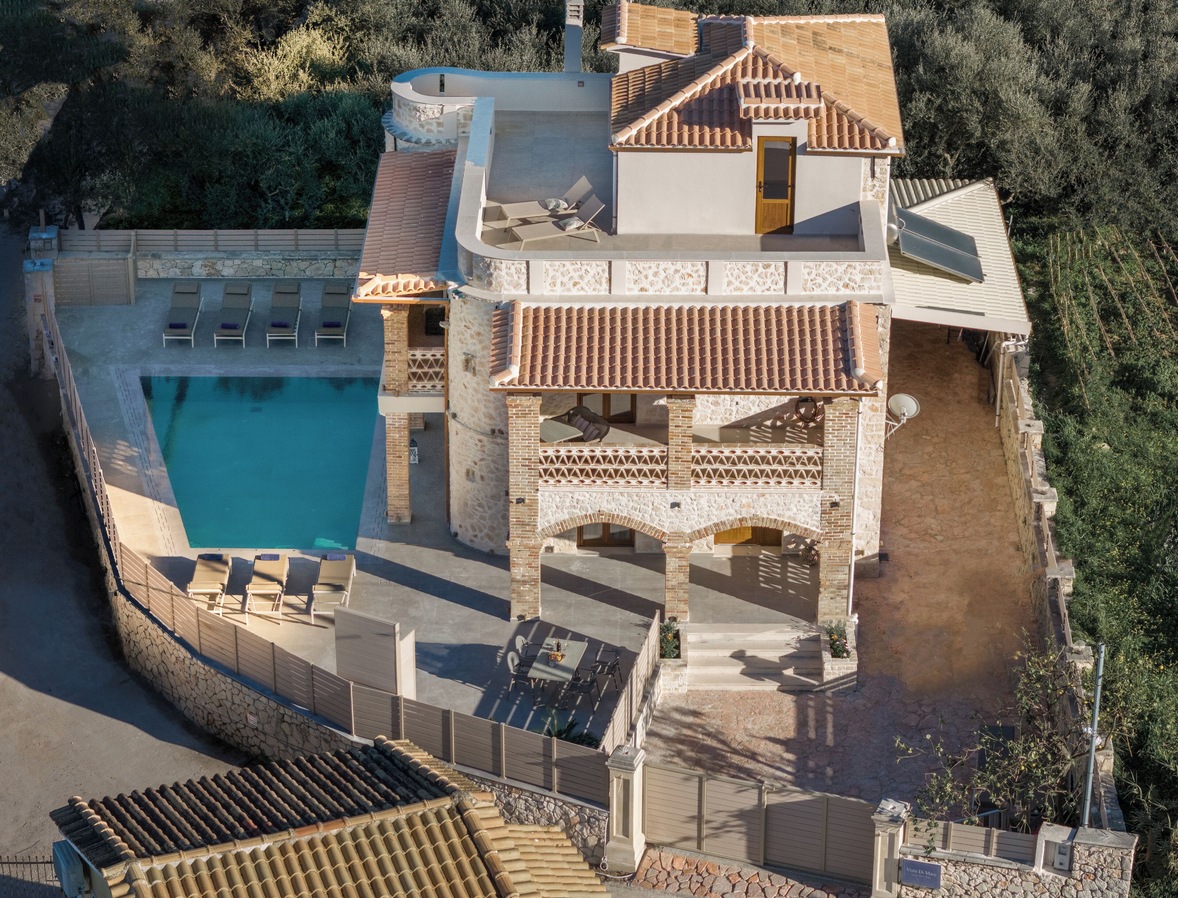 A large villa with a swimming pool, multiple terraces, and a stone facade.