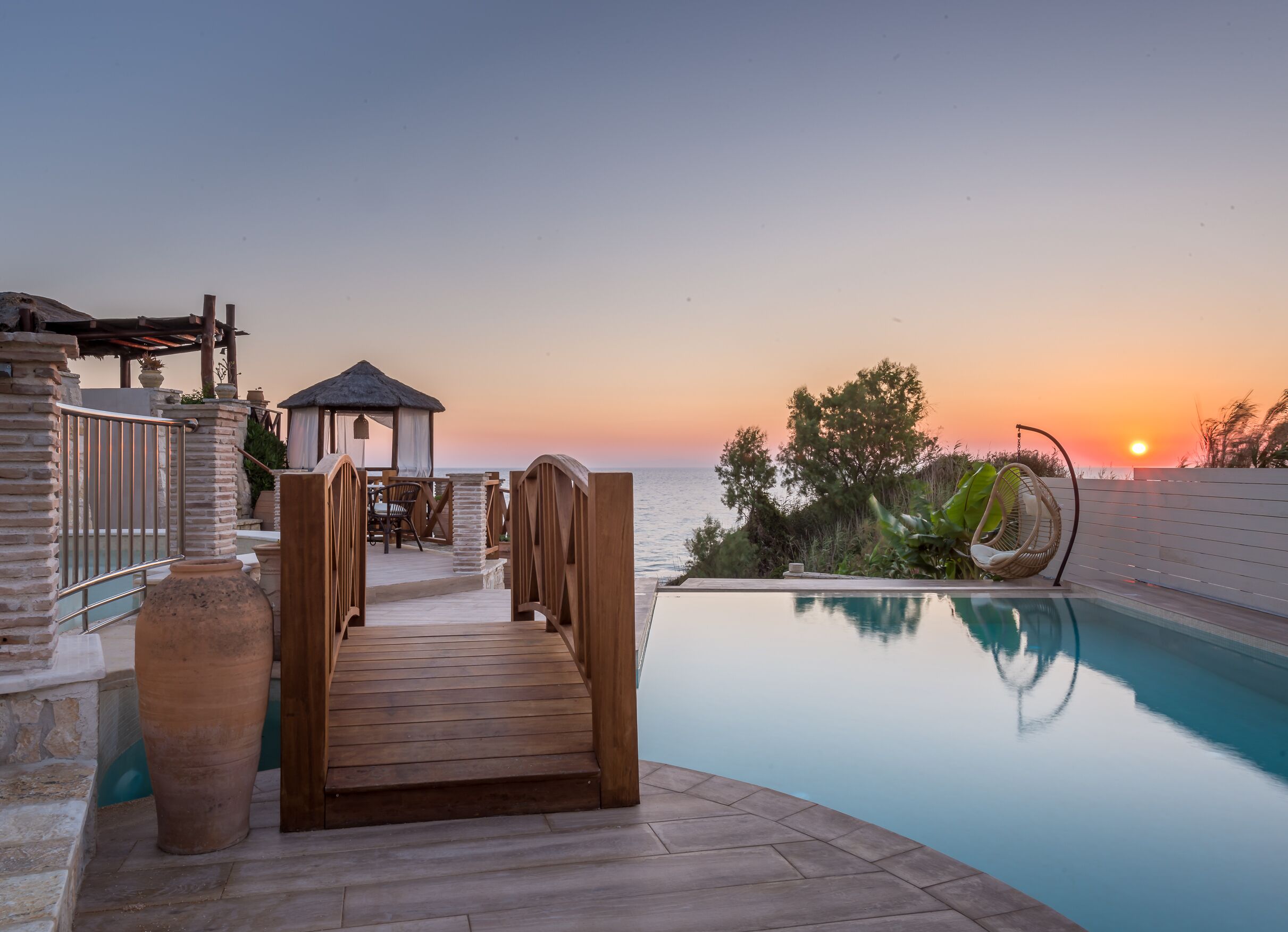 A wooden deck leading to a pool with a sunset view.