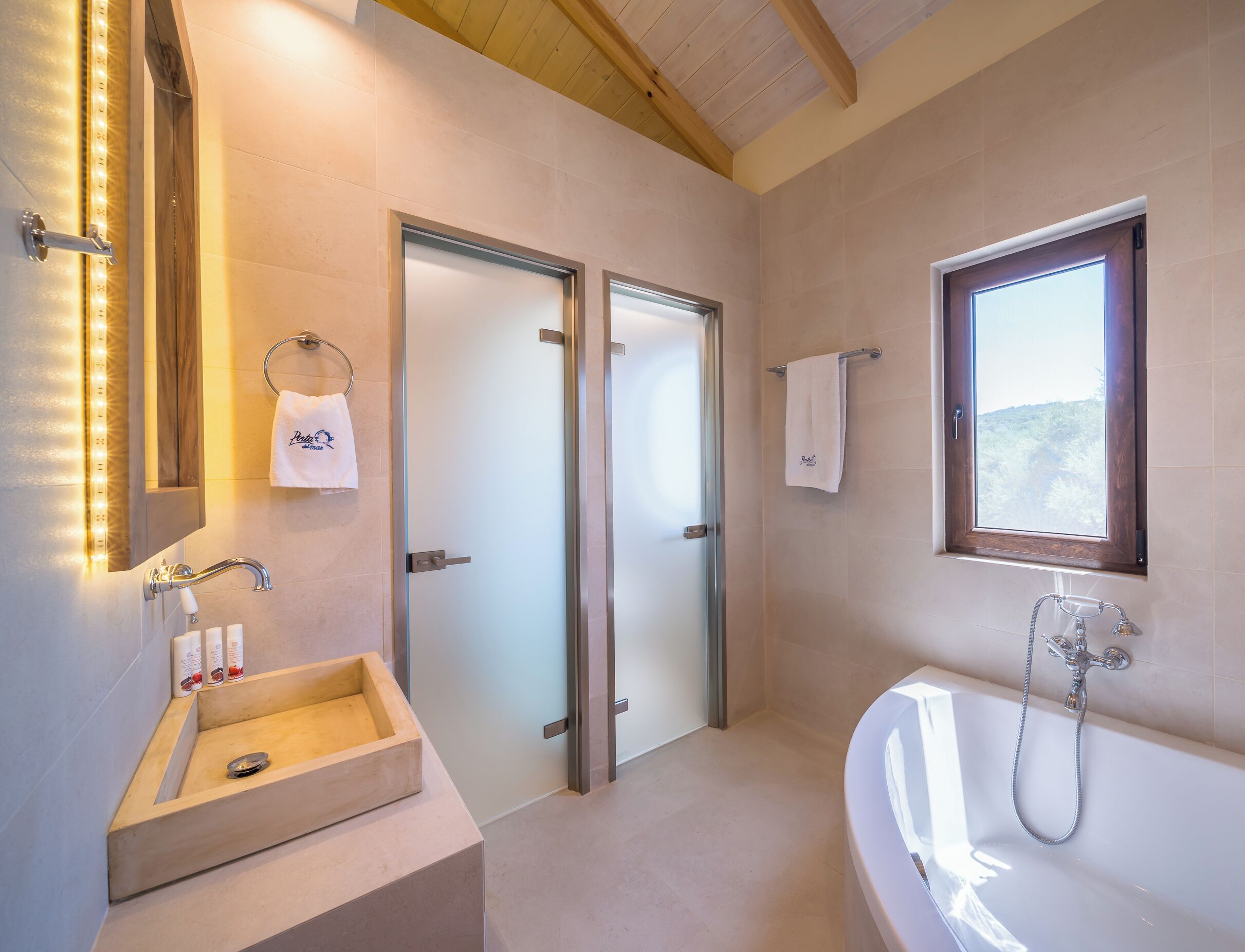 A modern bathroom with a freestanding bathtub, a glass-enclosed shower, a vanity with a wooden basin, and a large mirror with LED lights.