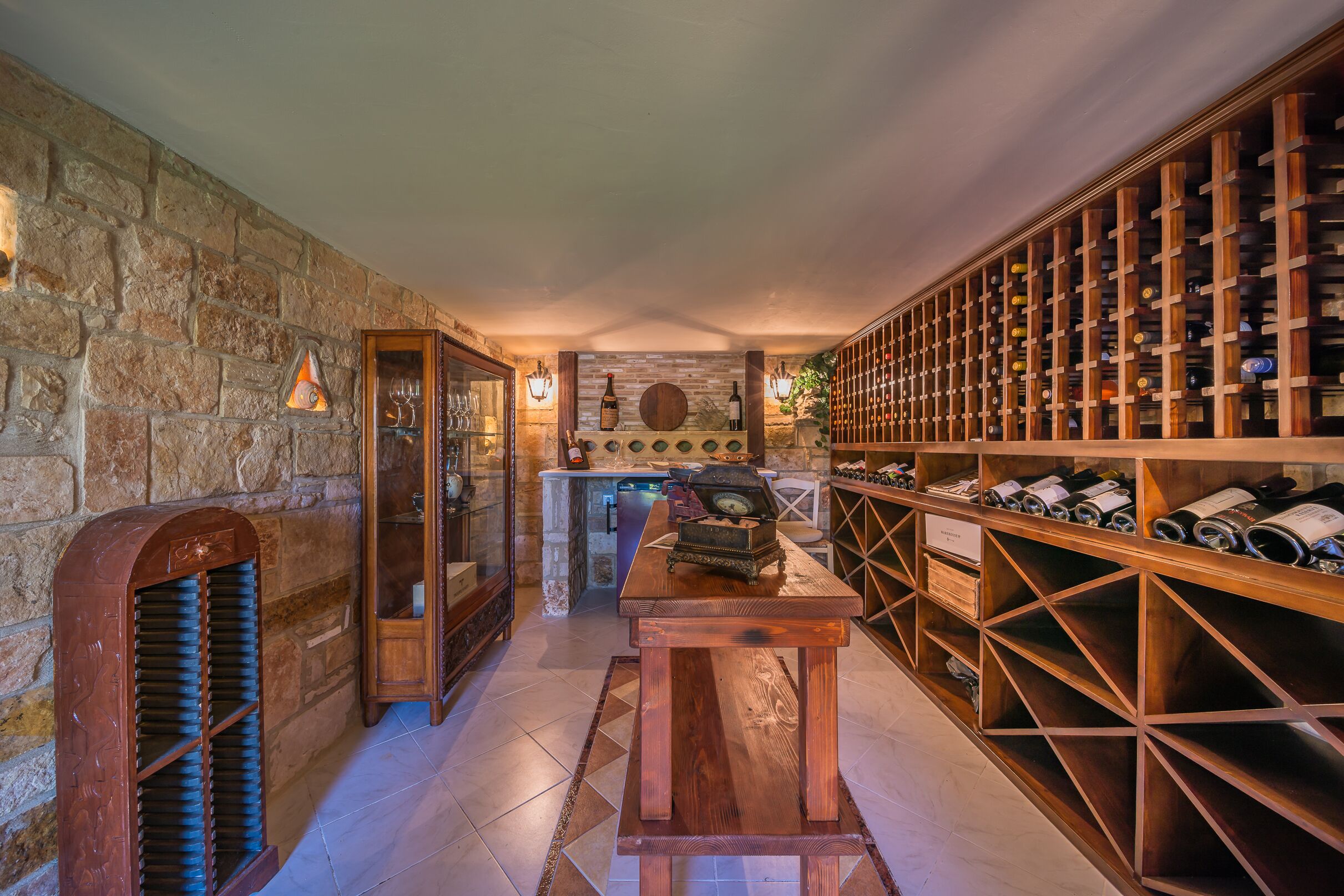 A wine cellar with stone walls, wooden wine racks, and a central table.