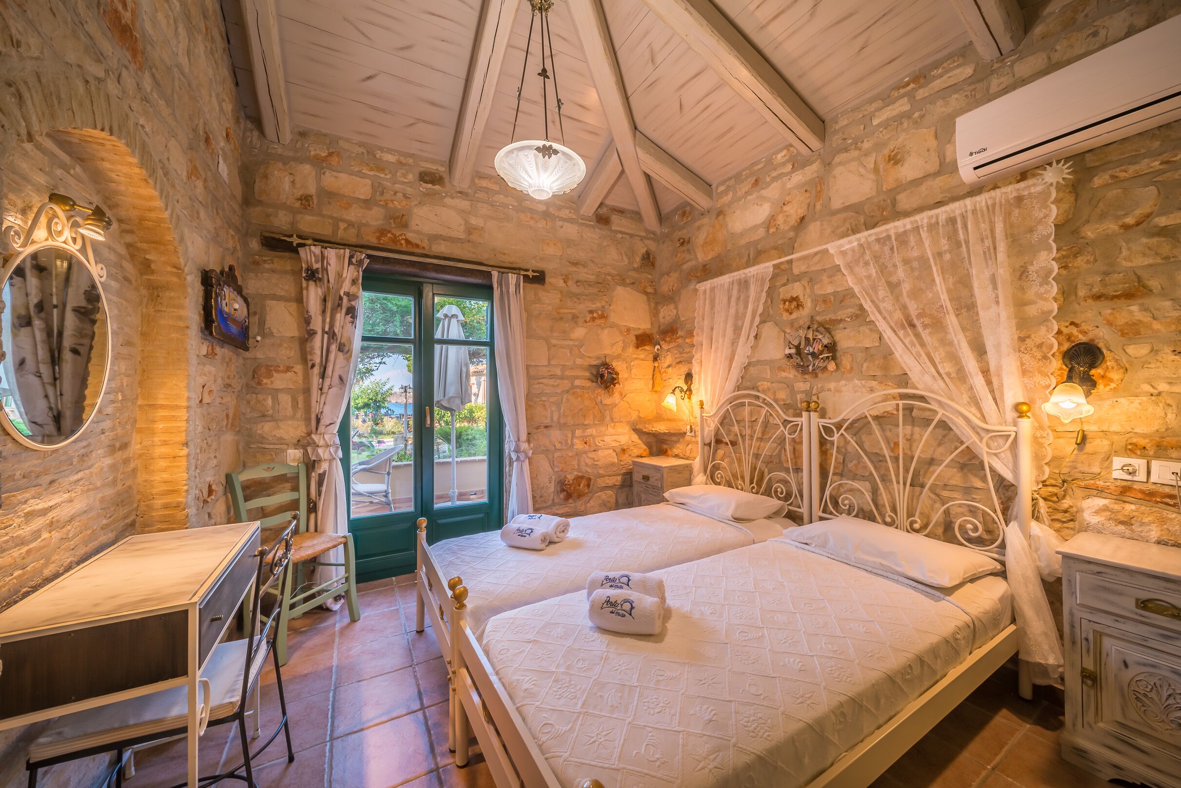 Un dormitorio con dos camas, un escritorio y una silla. Tiene una ventana con cortinas, un espejo y un aire acondicionado de pared.